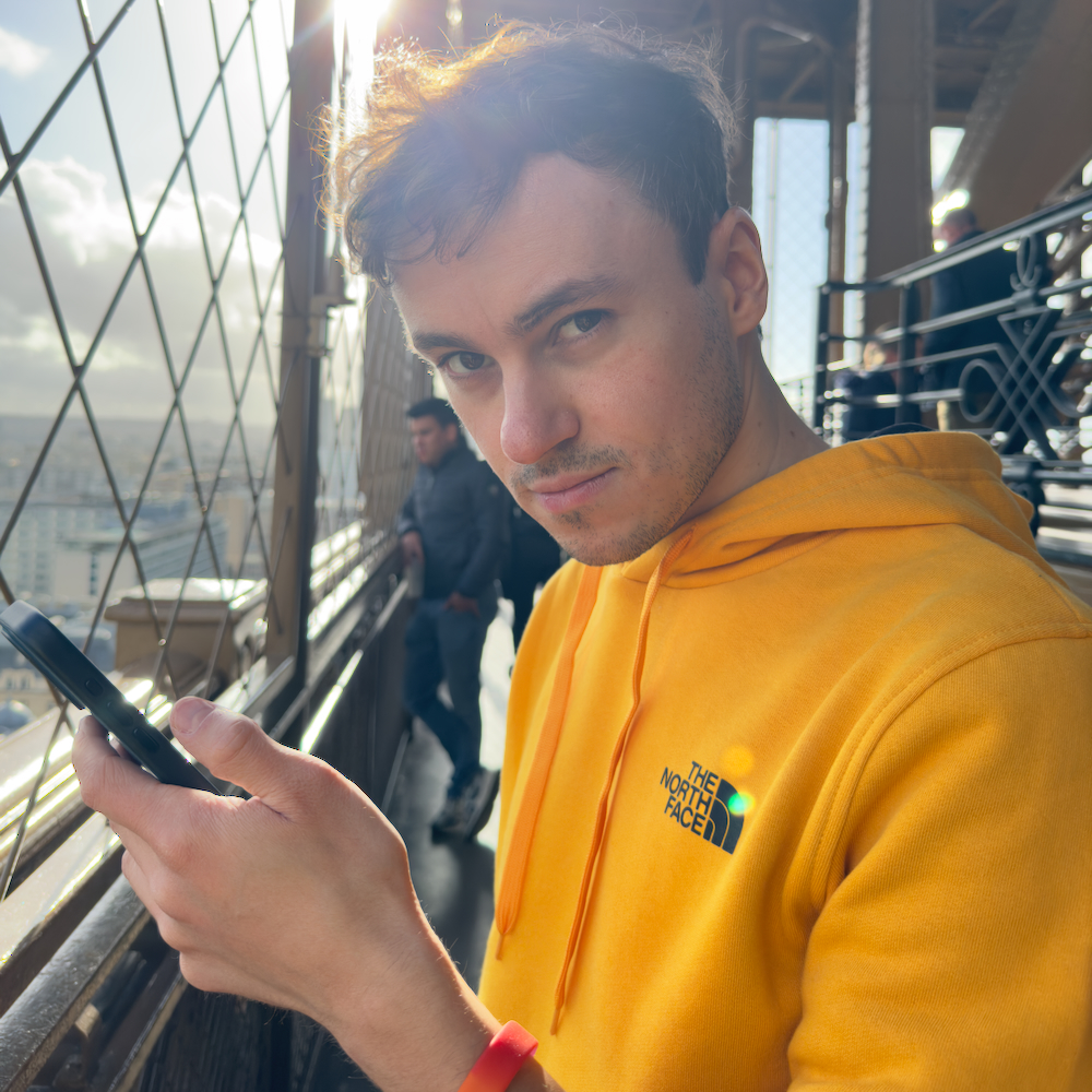 Lennart photographed from the left side, looking at the camera, holding an iPhone, atop the Eiffel tower